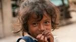 Young child with curly hair and a nose ring, smiling shyly.
